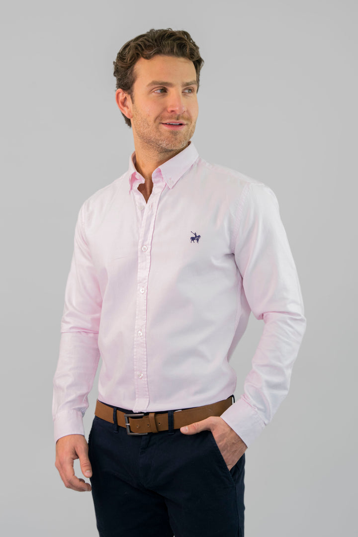 Camisa rosada hombre tipo Oxford. Modelo masculino vistiendo la camisa fajada, combinandola con un cinturón café y pantalón azul para un look formal.
