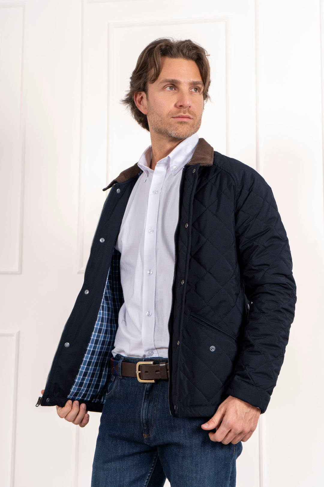 Chaqueta abierta, forro interior a cuadros azules. Prenda combinada con un jean azul oscuro y una camisa blanca para un look casual.