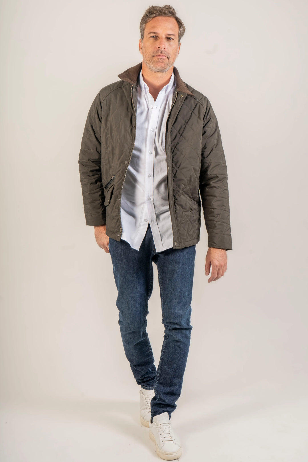 Modelo masculino de pie, usando la chaqueta en un look informal, junto con unos jeans azul oscuro y unos zapatos casuales blancos.